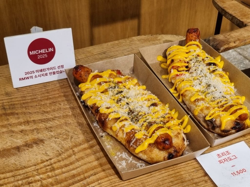 Two chorizo pizza dogs with mustard and grated cheese in paper trays at Amor Napoli Anguk