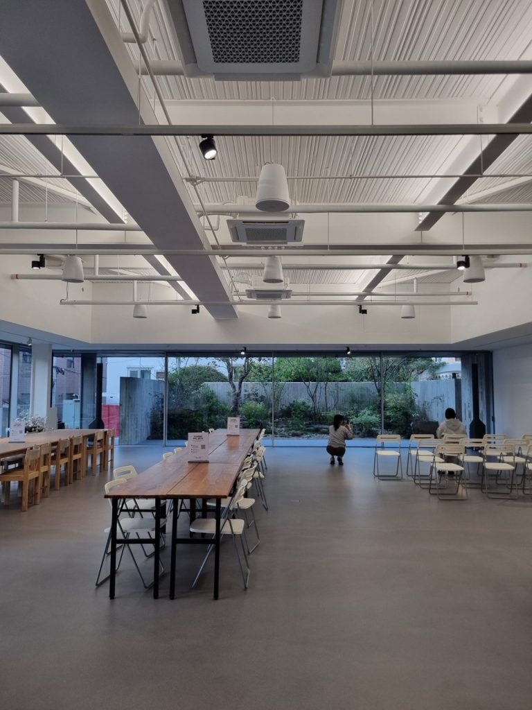 Bright first-floor lobby with long wooden tables facing a glass wall and garden