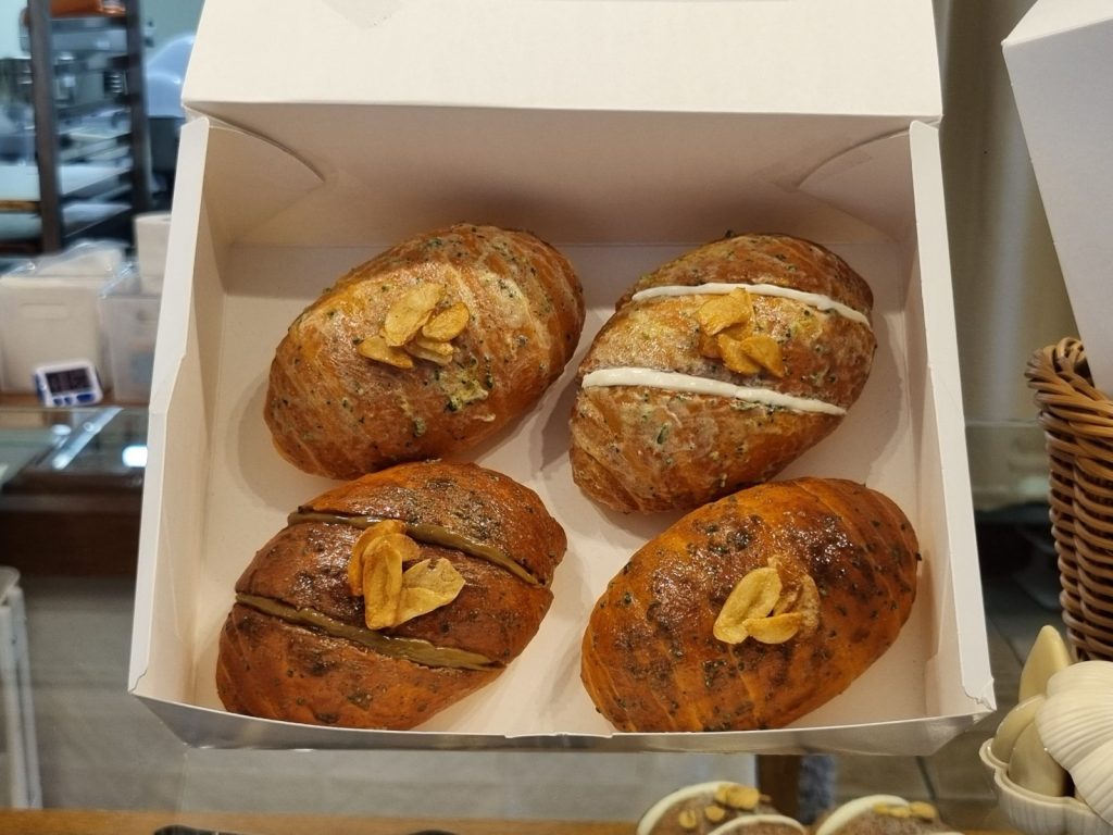 Box of four garlic salt breads topped with garlic chips, including garlic cream cheese and black garlic versions